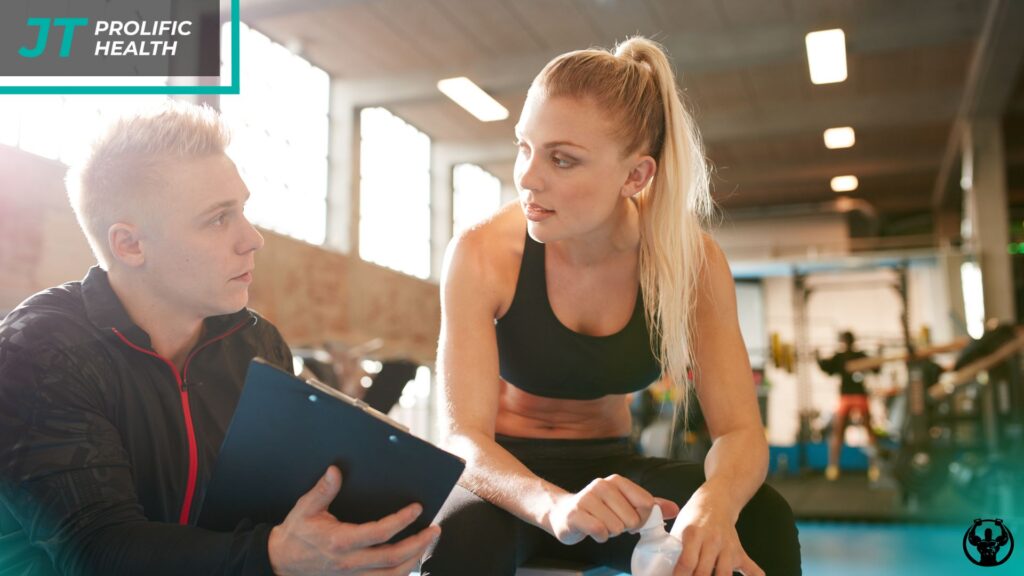 Trainer discussing fitness goals with a client in a gym setting, emphasizing personalized assessments and health strategies at Prolific Health.